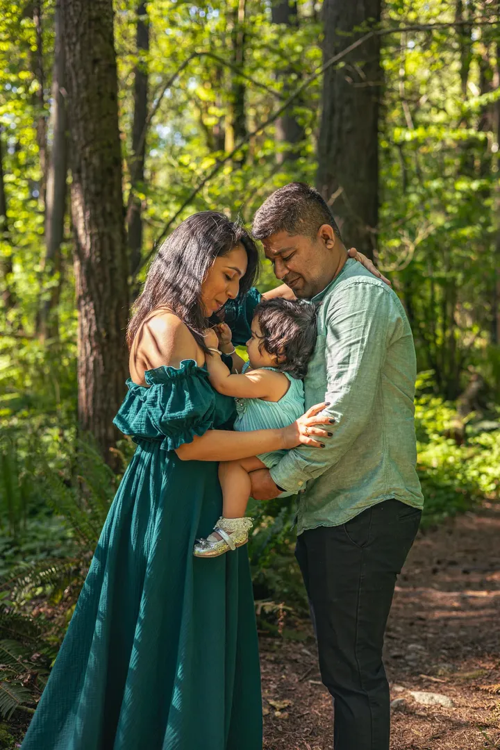 Child standing in forest beside mother resting in a tree during soulful family session.